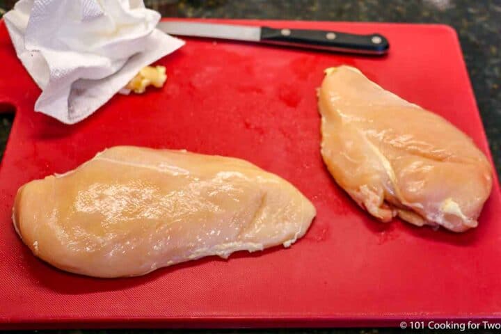 trimming chicken breasts on a red board.