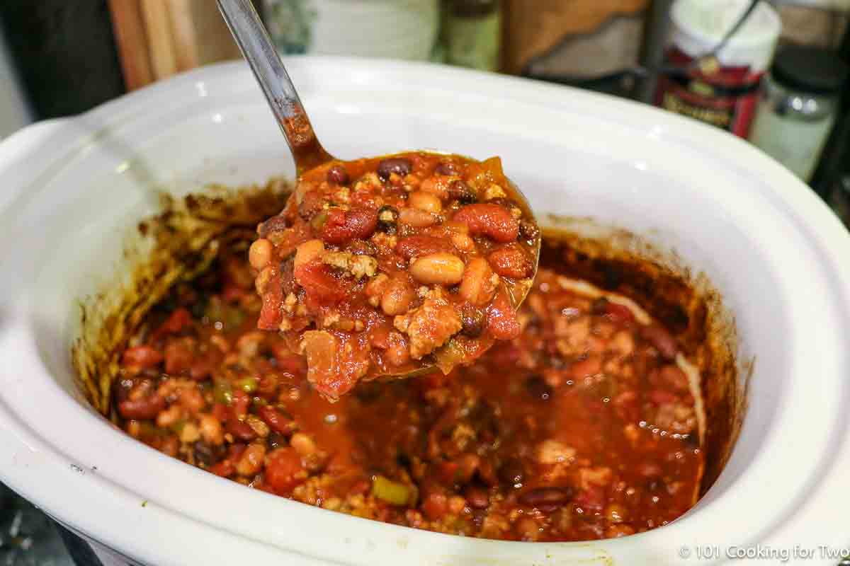 Ladle full of turkey chili over a crock pot.