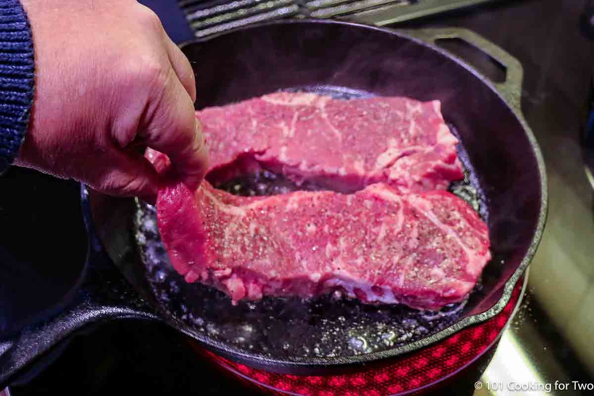 adding strip steaks to the hot pan.