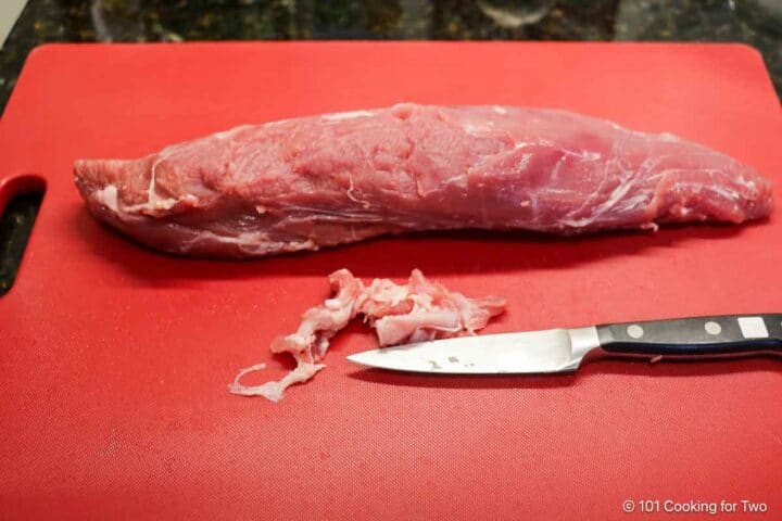 trimmed pork tenderloin on a red board.