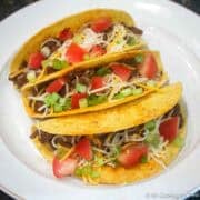 Three hard shell spicy tacos on a white plate.