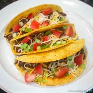 Three hard shell spicy tacos on a white plate.