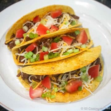 Three hard shell spicy tacos on a white plate.