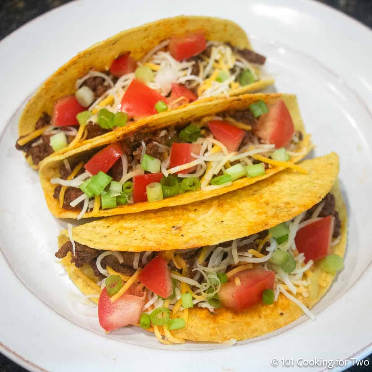 Three hard shell spicy tacos on a white plate.