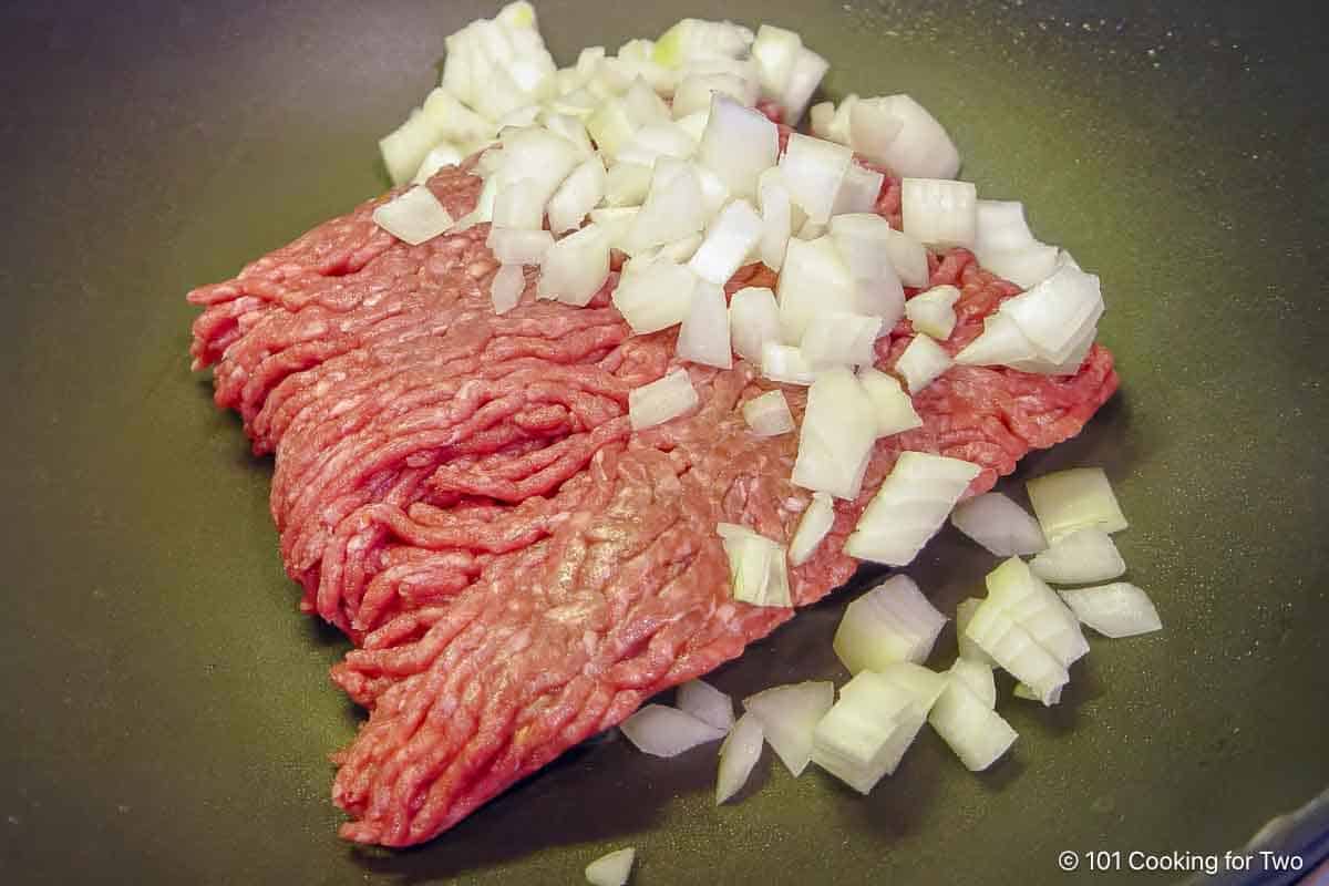raw burger and chopped onion in skillet.