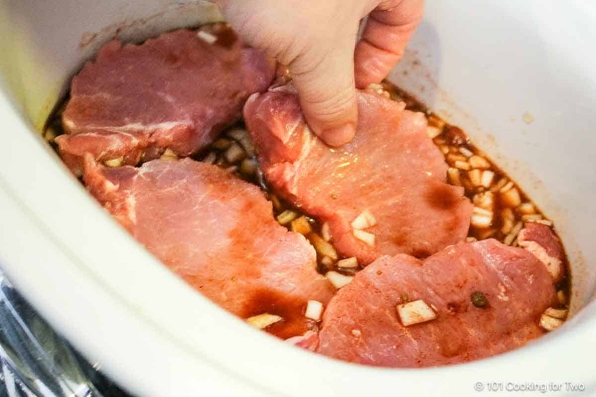 adding pork slices to crock pot.