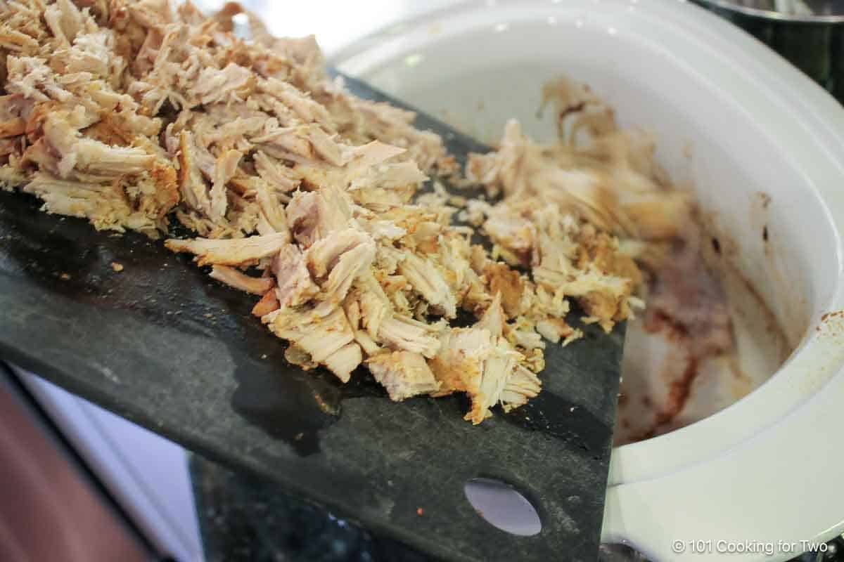 pouring shredded pork back into crock pot.