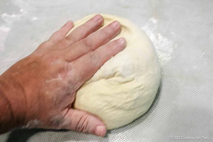 hand-kneading dough ball on a floured surface.