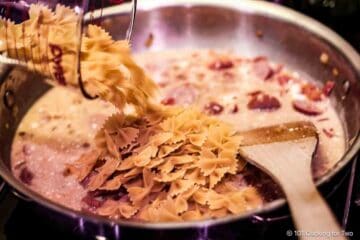 Adding bowtie pasta to the pan.