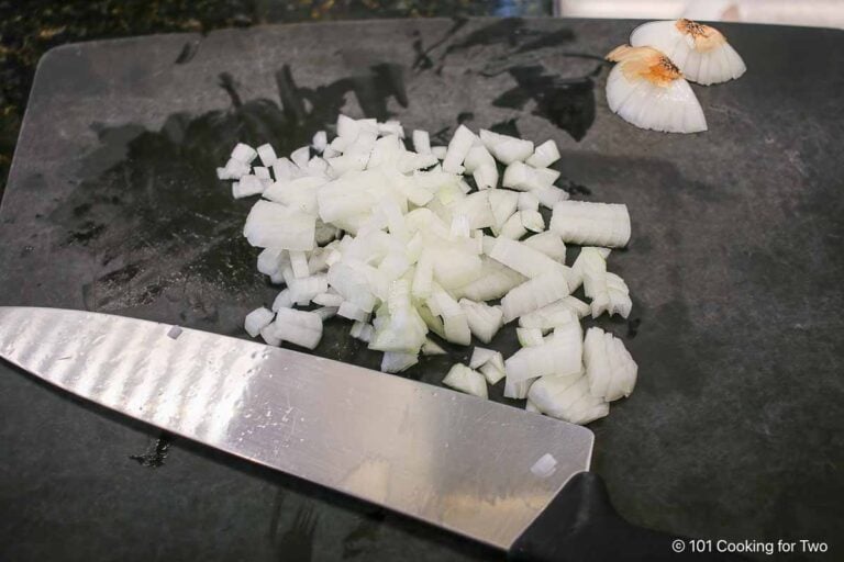 A chopped onion on a black board with a knife.
