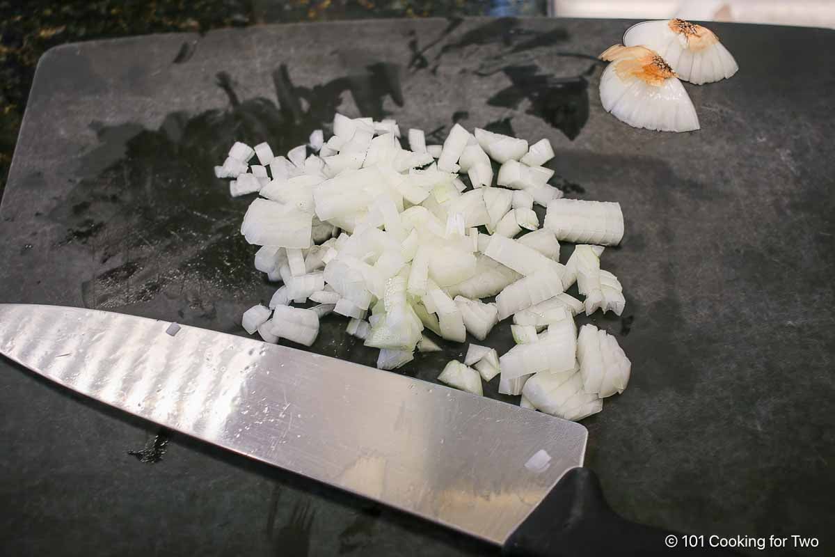 A chopped onion on a black board with a knife.