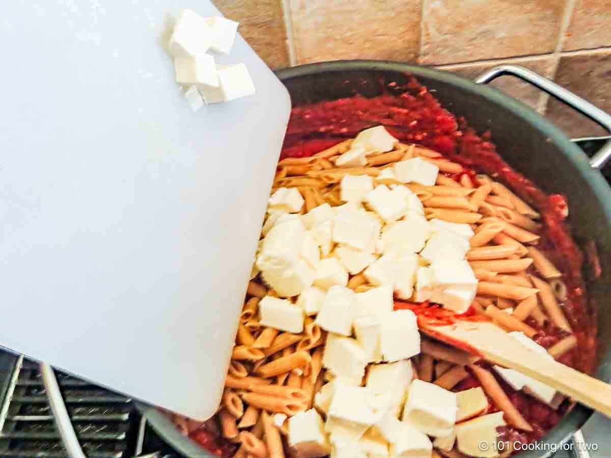 Mixing pasta and cheese cubes into the sauce.