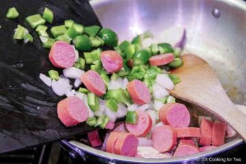 Adding vegetables and sausage to the skillet with the chicken.