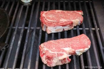 Ribeye steaks on the grill grates.