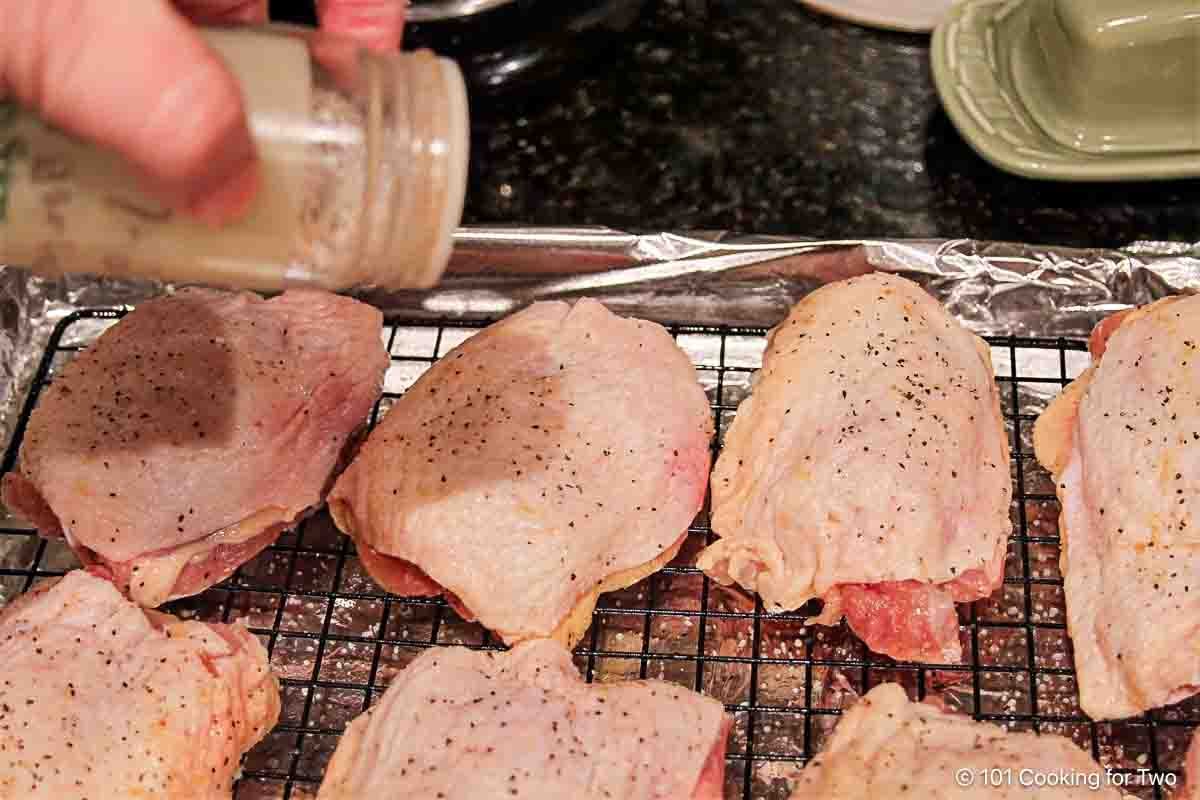 Seasoning raw chicken thighs on a tray with a rack.