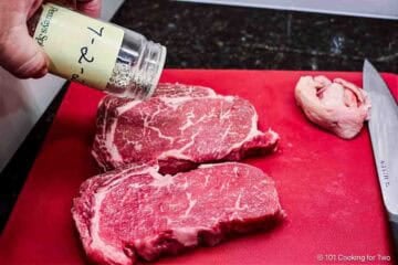 Seasoning ribeye steaks.