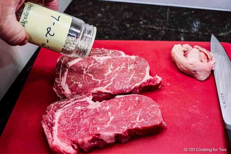 Seasoning ribeye steaks.