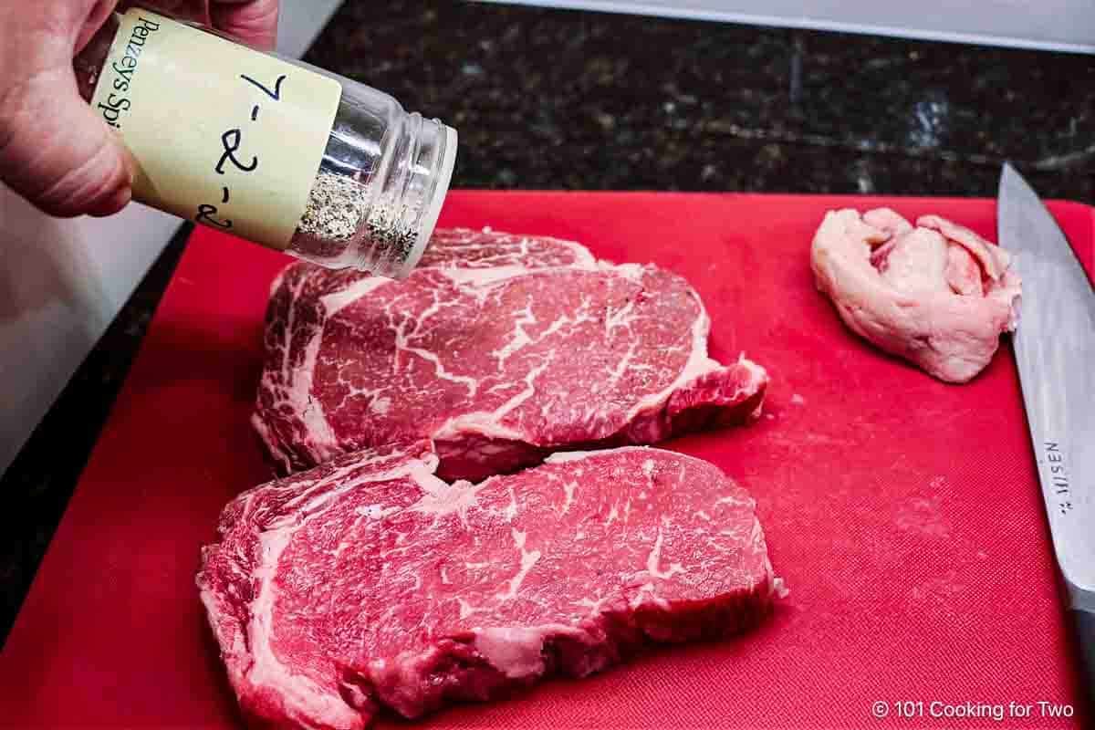 Seasoning ribeye steaks.