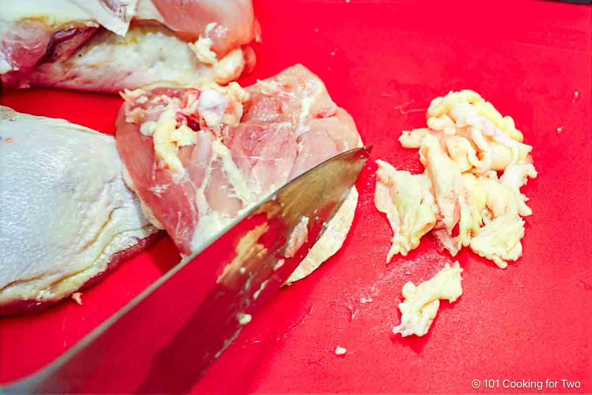 Trimming raw chicken thighs of fat and extra skin.