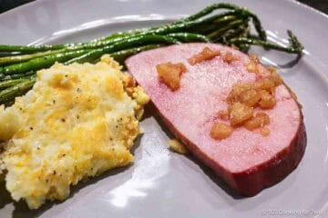 Slice of ham with pineapple and side dishes.