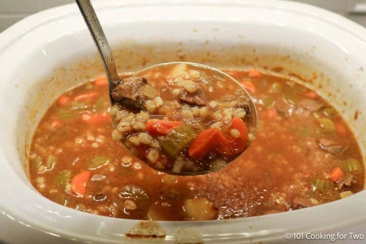 Beef barley soup in a ladle over a crock pot.