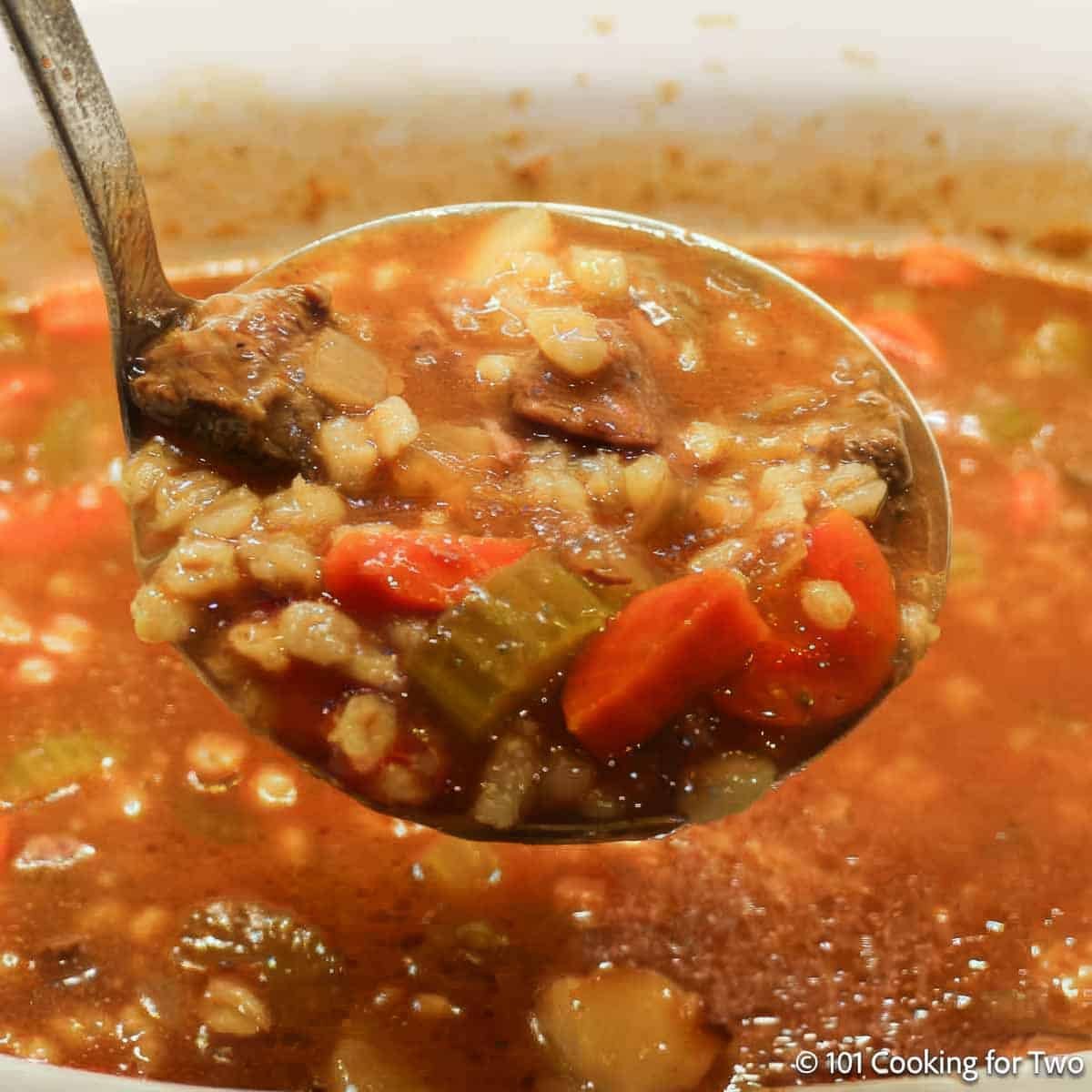 Ladle of beef barley soup over a crock pot.