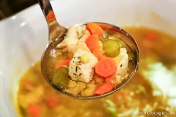 A ladle full of chicken vegetable soup in a slow cooker.