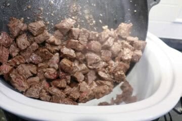 Adding browned meat to the crock pot.