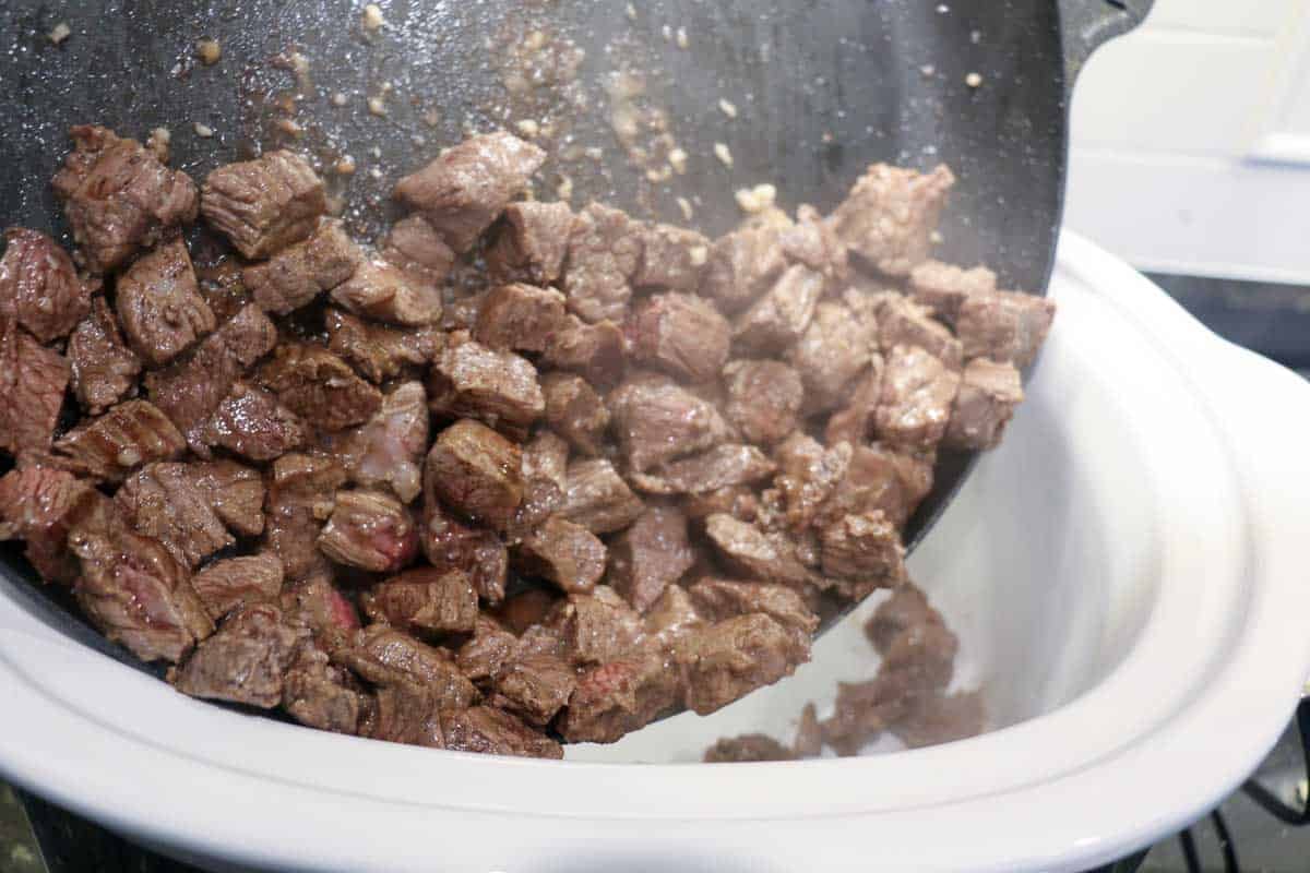 Adding browned meat to the crock pot.
